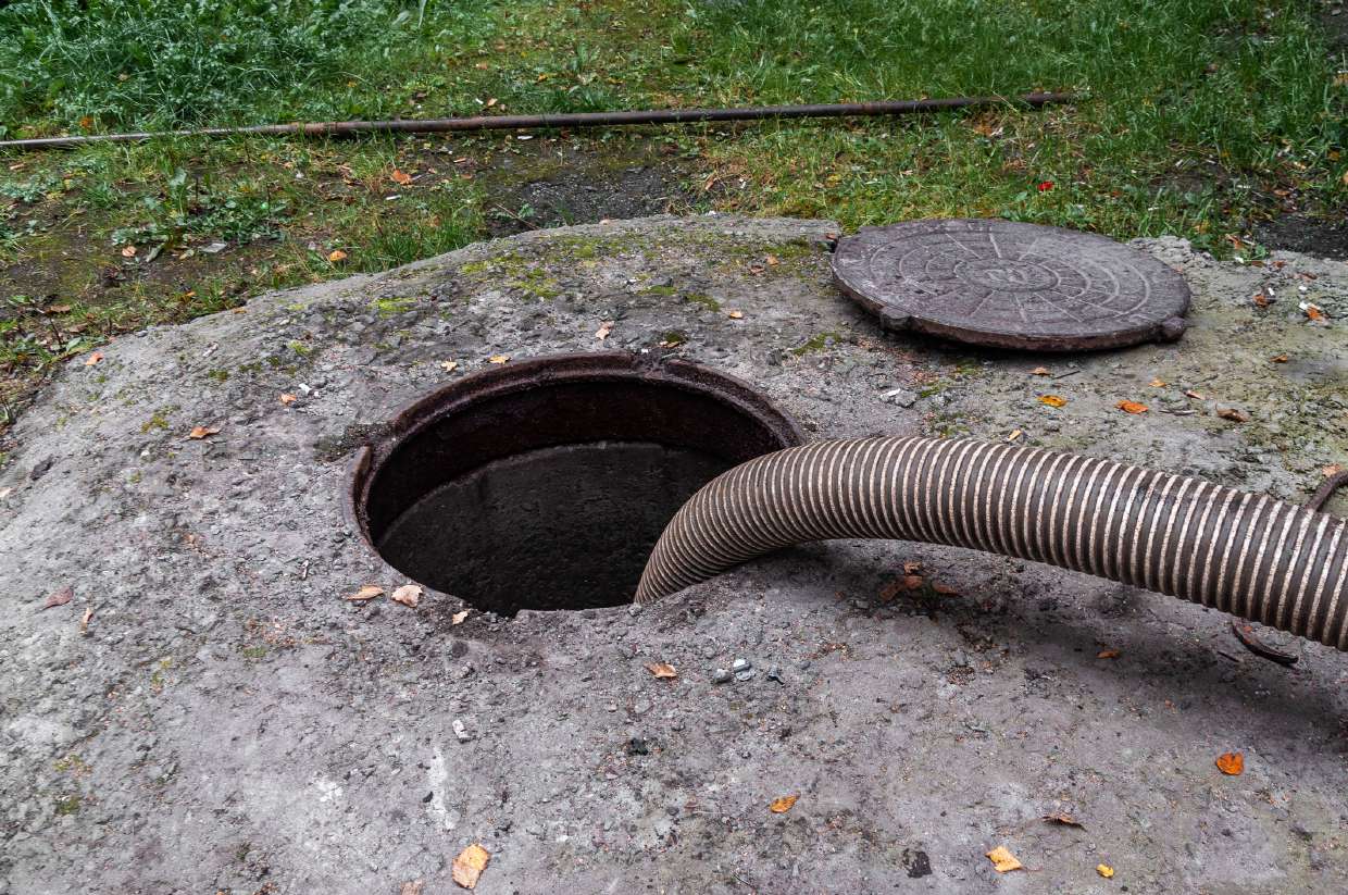 Septic Inspection in Kingston, NY — Open septic manhole in a lawn with a pump-out hose